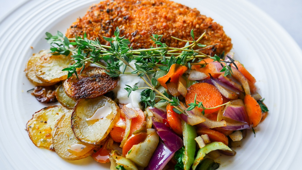 Sprø og saftig svinesnitzel med potetskiver og ovnsbakte grønnsaker.